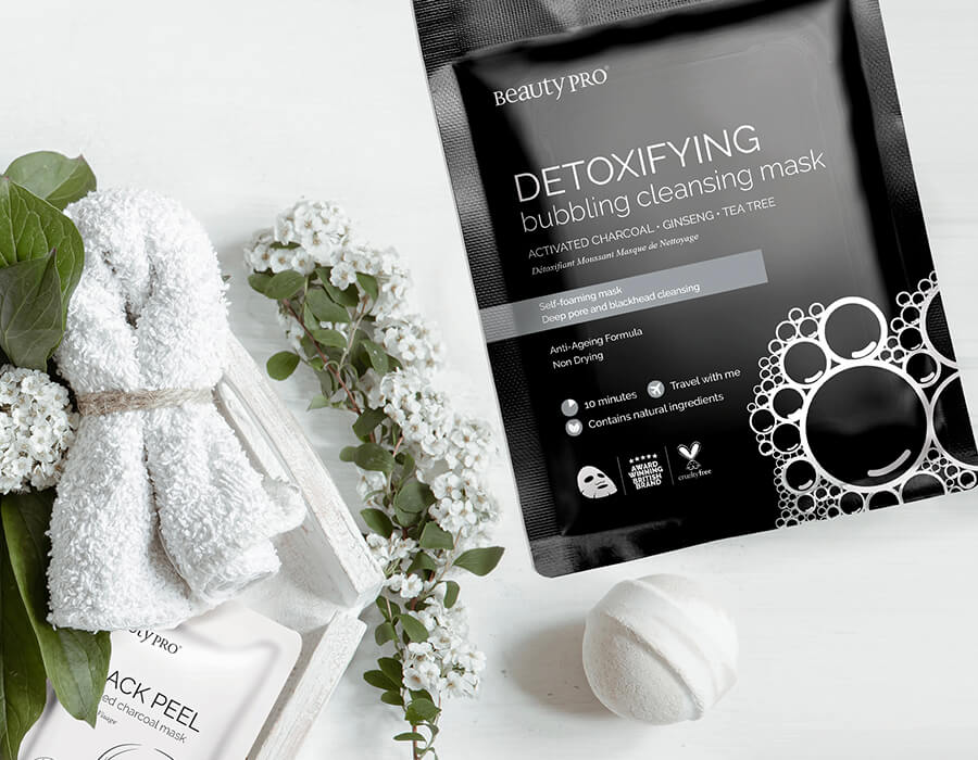 The detoxifying mask packaging on a white backgrop with a white flannel, bathbomb and face cloth.